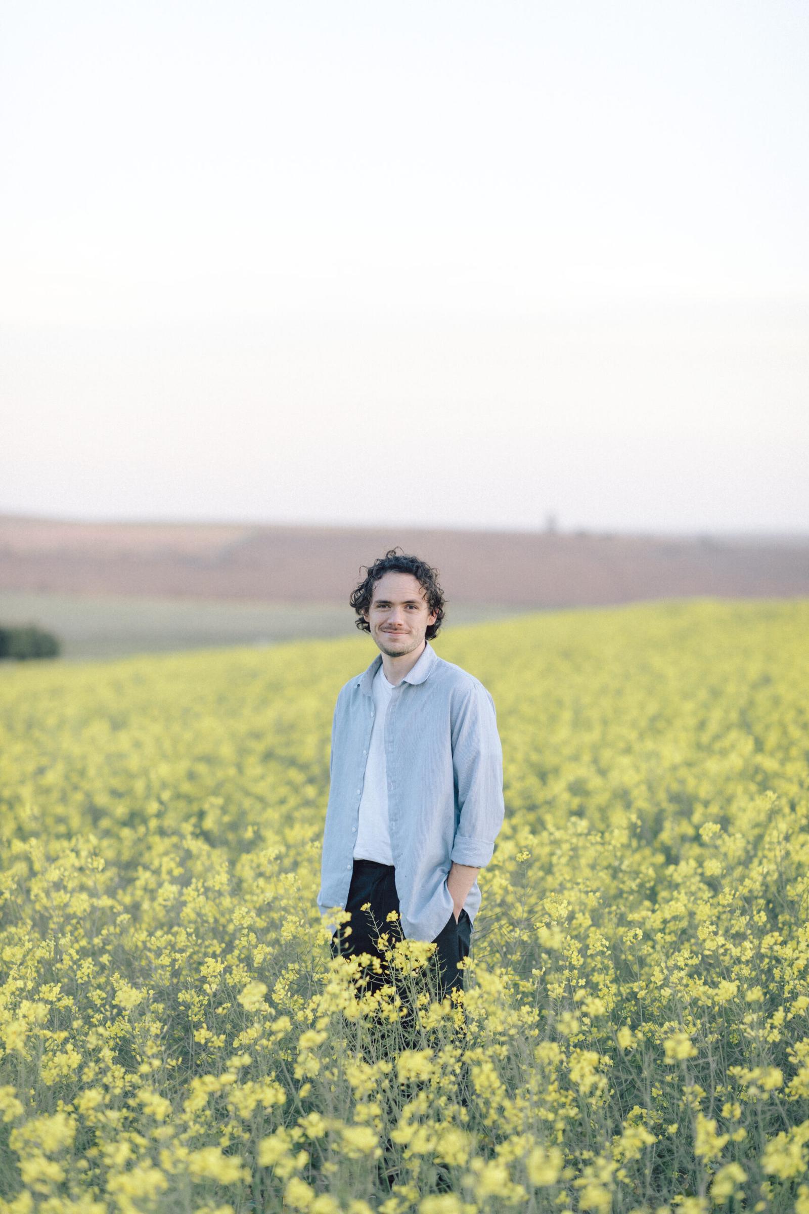 Cape Town wedding photographer. Damian Van Der Walt, stands in a field of yellow canola flowers