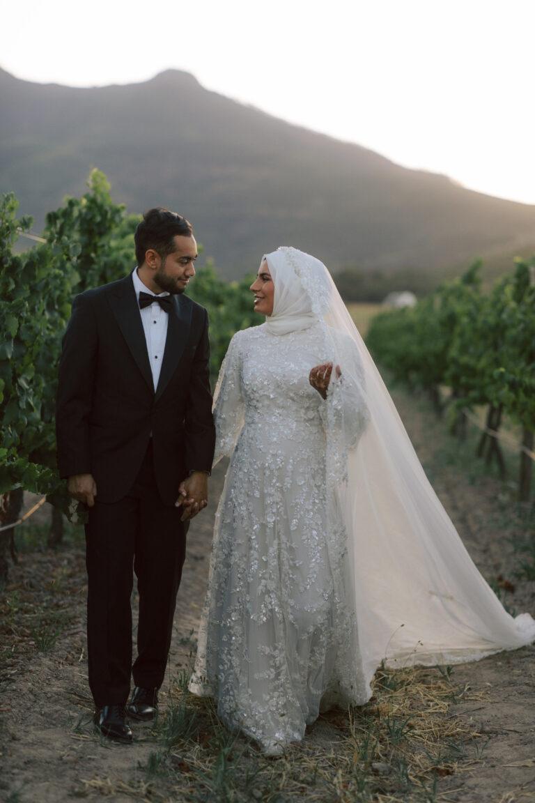 Bride and Groom walking down a vineyard isle at sunset