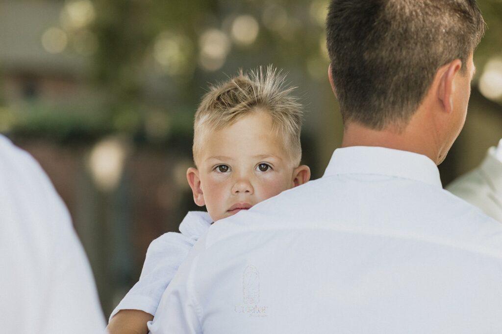 Young boy looking over dad's shoulder at a wedding