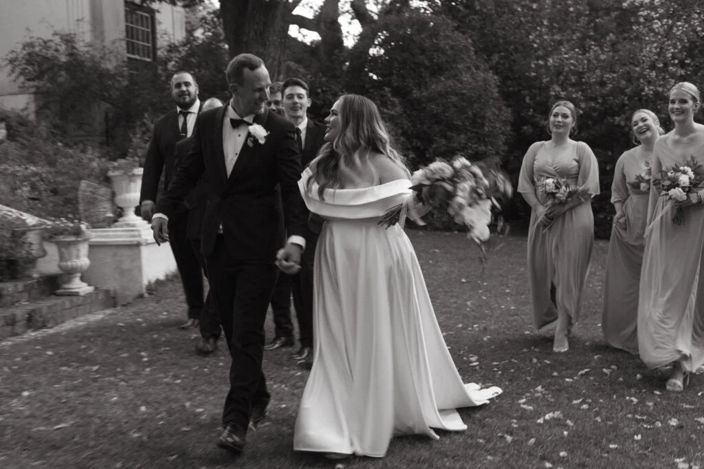 black and white image of a bride and groom walking past their wedding party