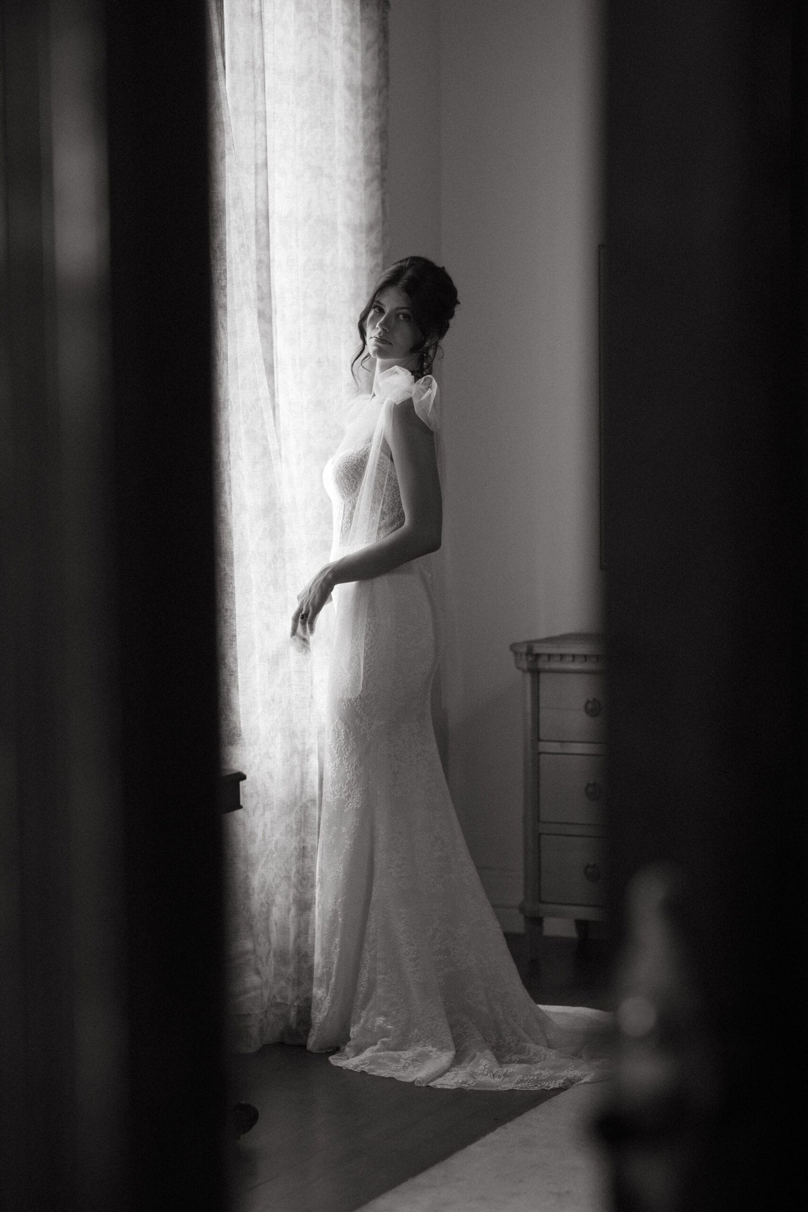 Bride in wedding gown standing in the tall window light inside Steenberg estate's manor house