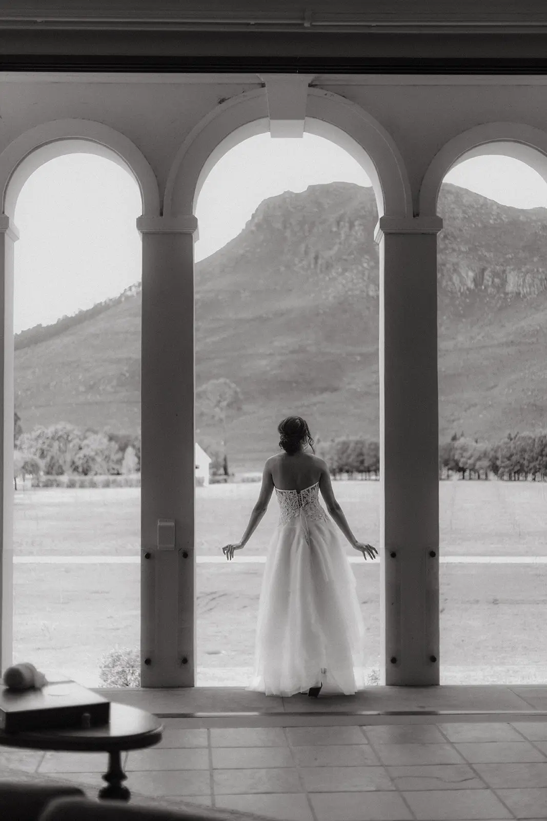 Black and white of a bride in La Roche's manor house looking towards the mountains.