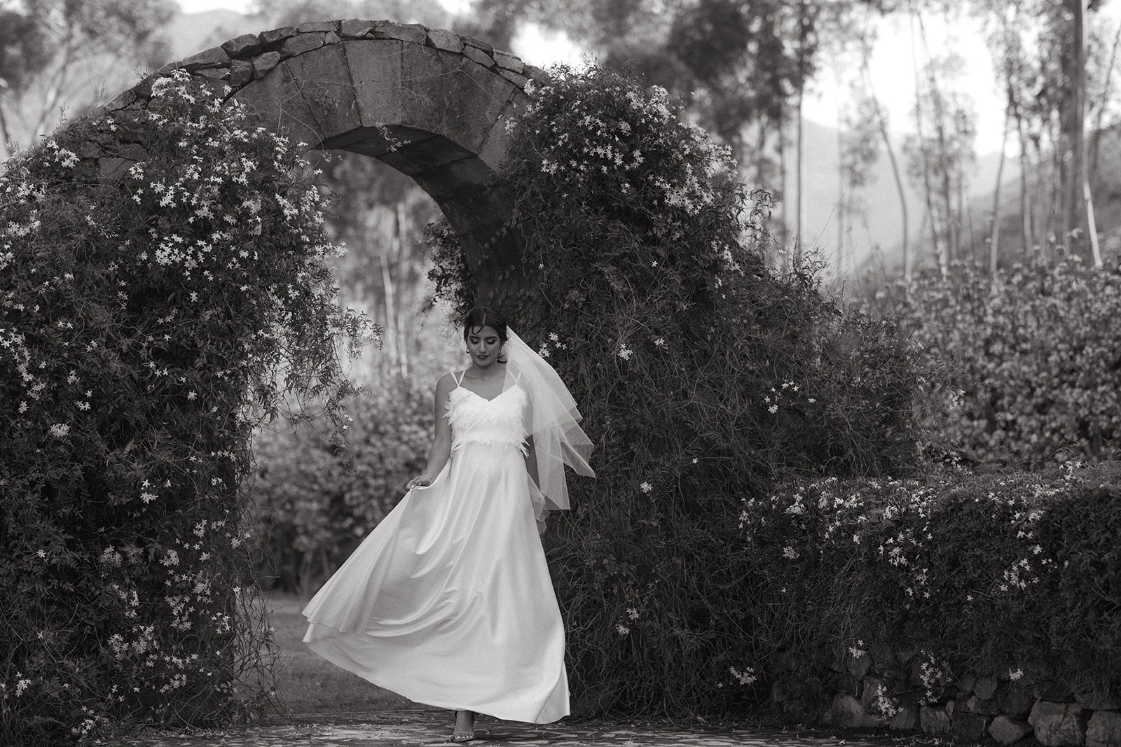 Black and white of a bride beneath a stone arch with jasmine at La Roche Estate