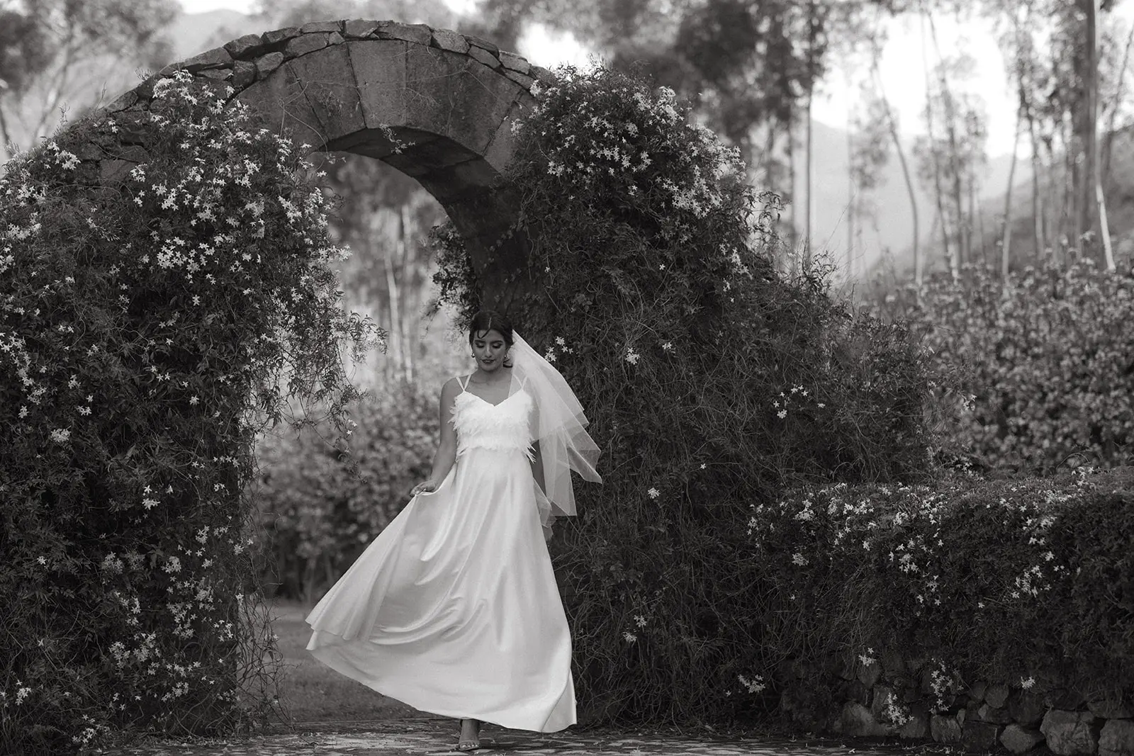 Black and white of a bride beneath a stone arch with jasmine at La Roche Estate