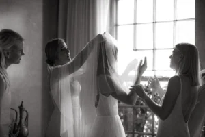 Black and white wedding image of a bride with her bridesmaids helping her fix her veil.