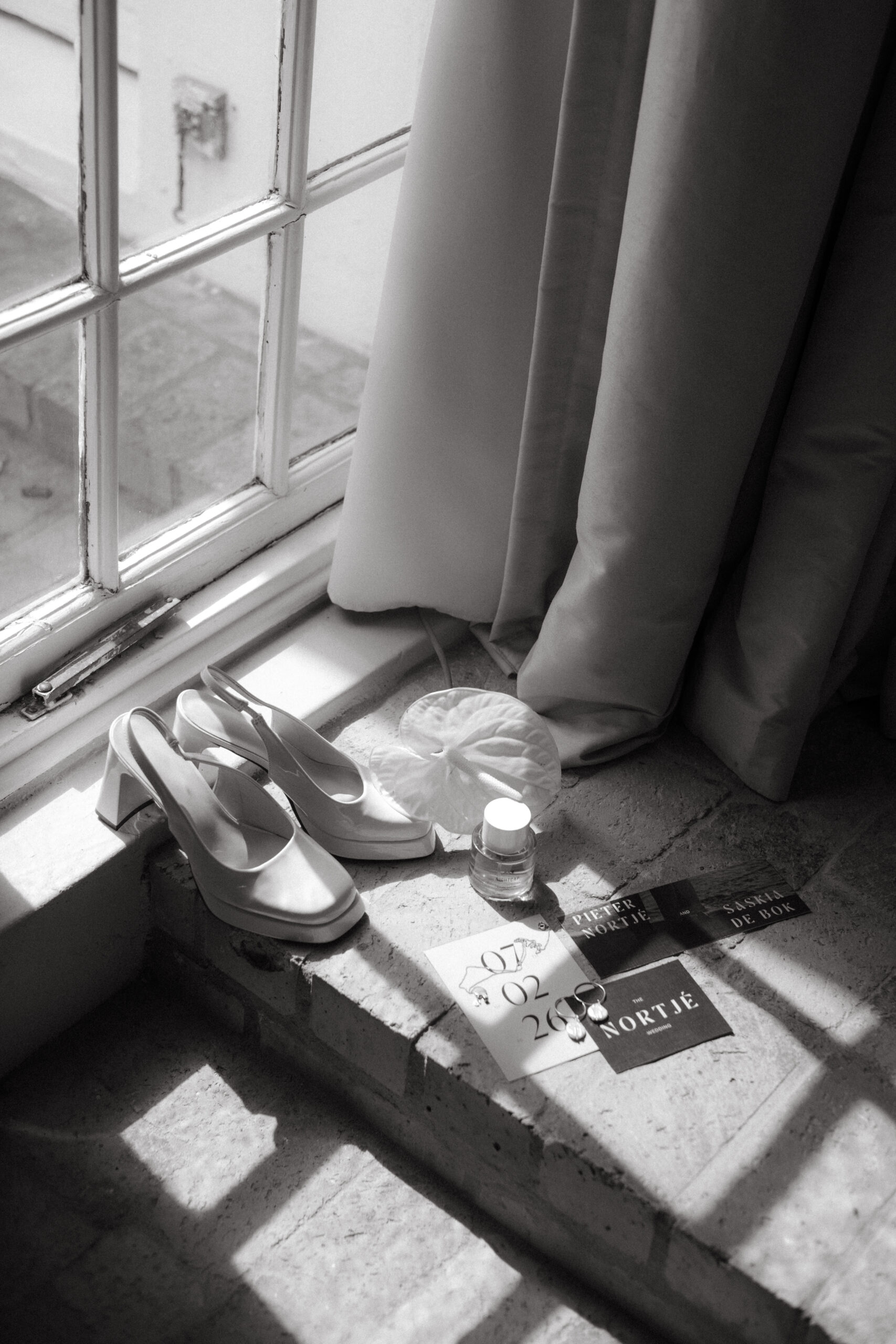 Wedding details image showing shoes, rings and other details by a window.