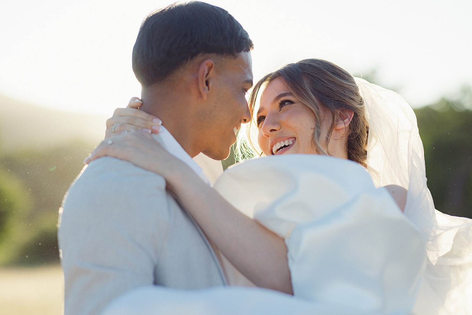 A close up of a backlit wedding couple. The bride is being carried in the grooms arms.