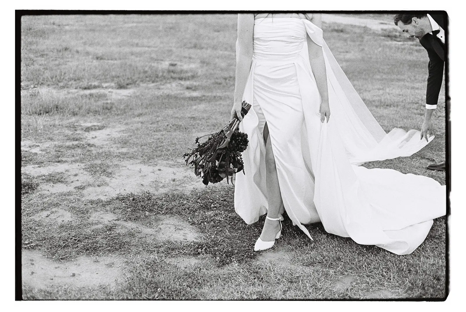 Black and white film image of a groom fixing his bride's dress