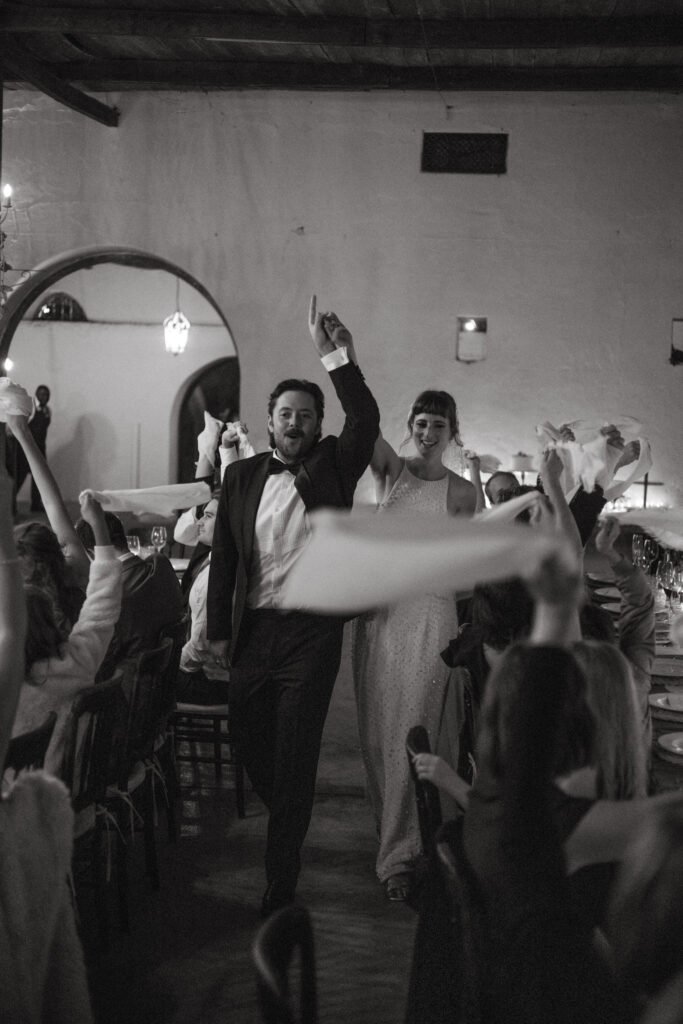 Wedding couple walking into their reception area to waving napkins
